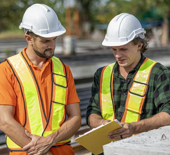 Two logistics team members in safety vests reviewing documents