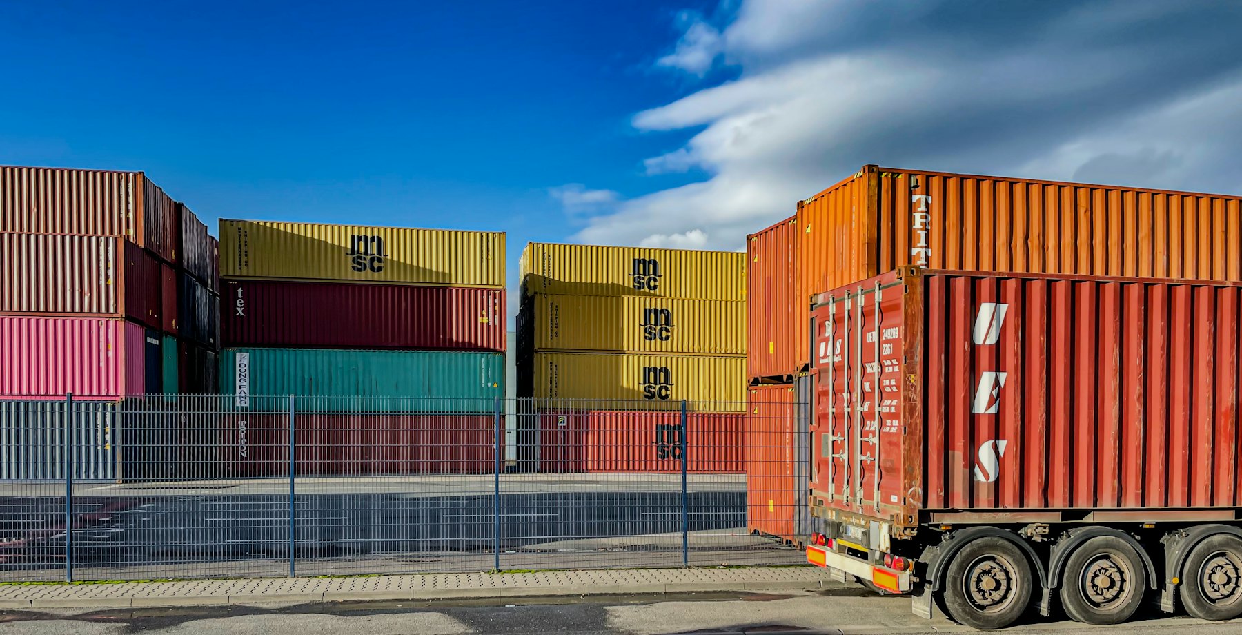 Container truck driving past stacked shipping containers