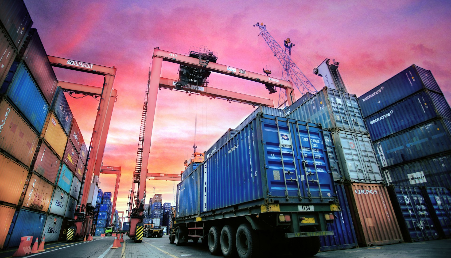 Stacked shipping containers at a busy port at sunset